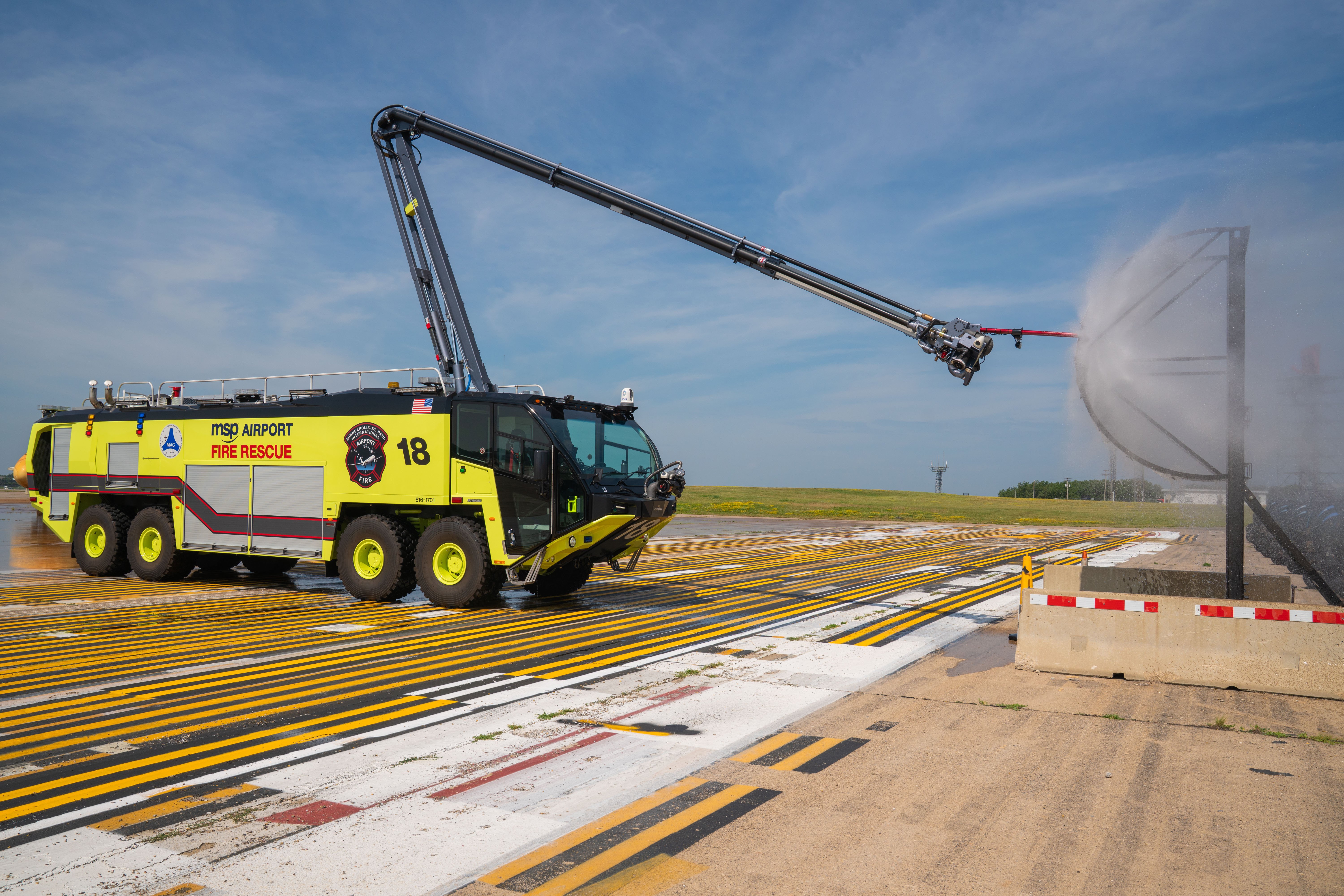 A Striker 8x8 ARFF spraying water from the Snozzle high reach extendable turret on a sunny day.