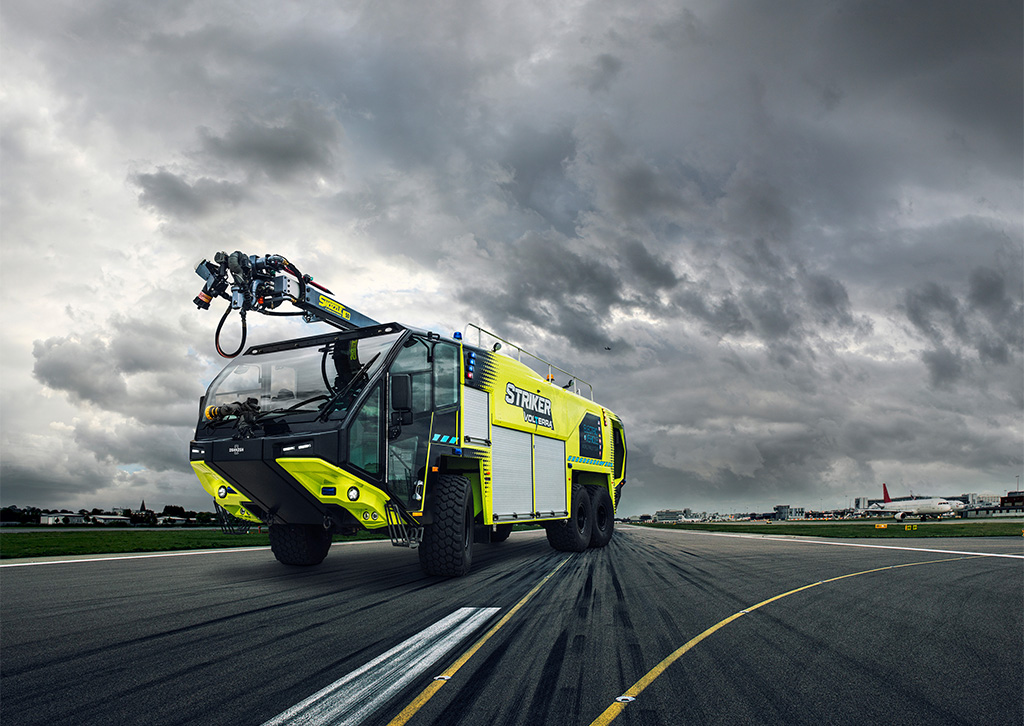 Yellow Striker Volterra hybrid electric ARFF truck parked on airport runway underneath stormy, overcast skies
