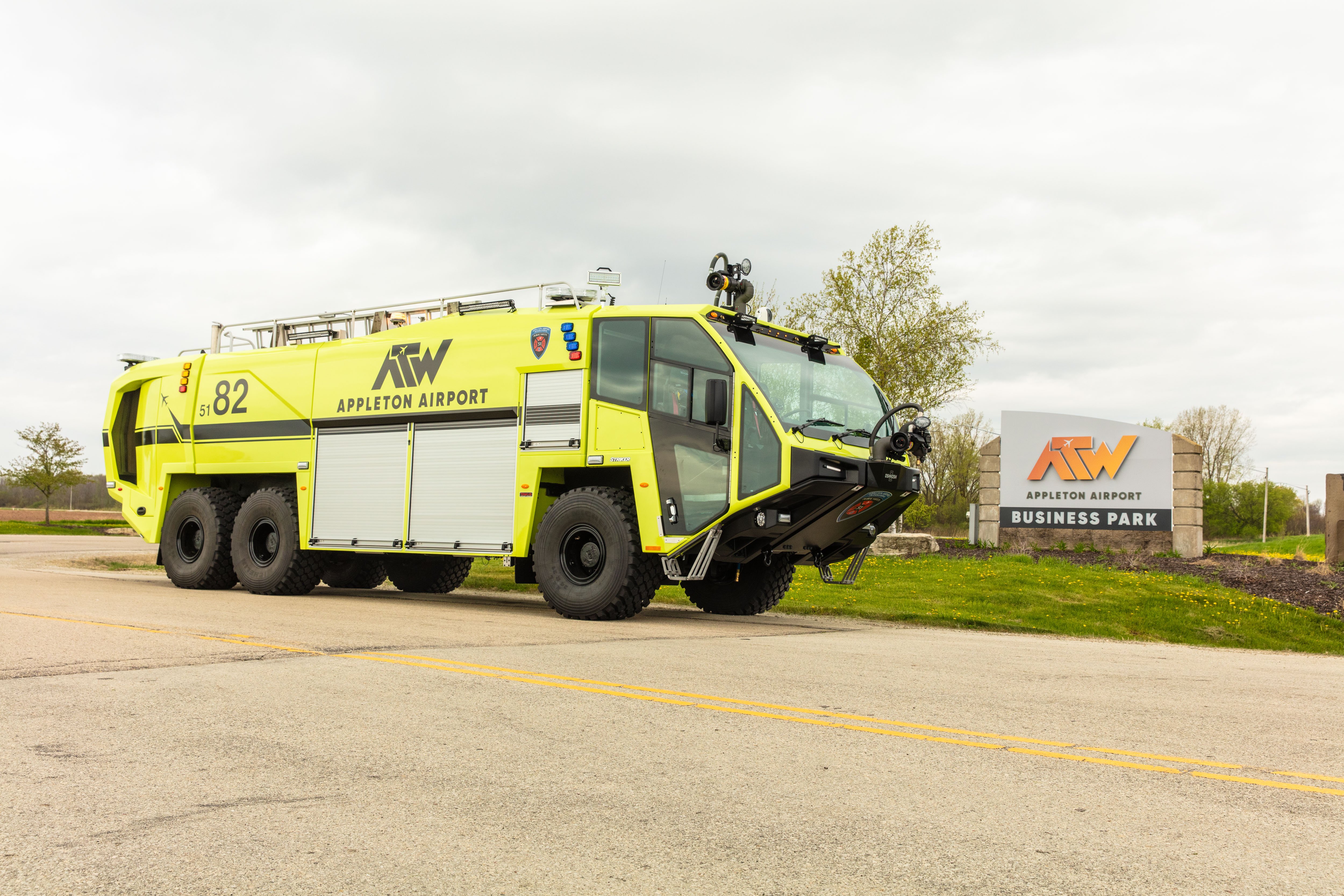 A Striker 6x6 ARFF parked outside near the Appleton International Airport sign on a cloudy day.