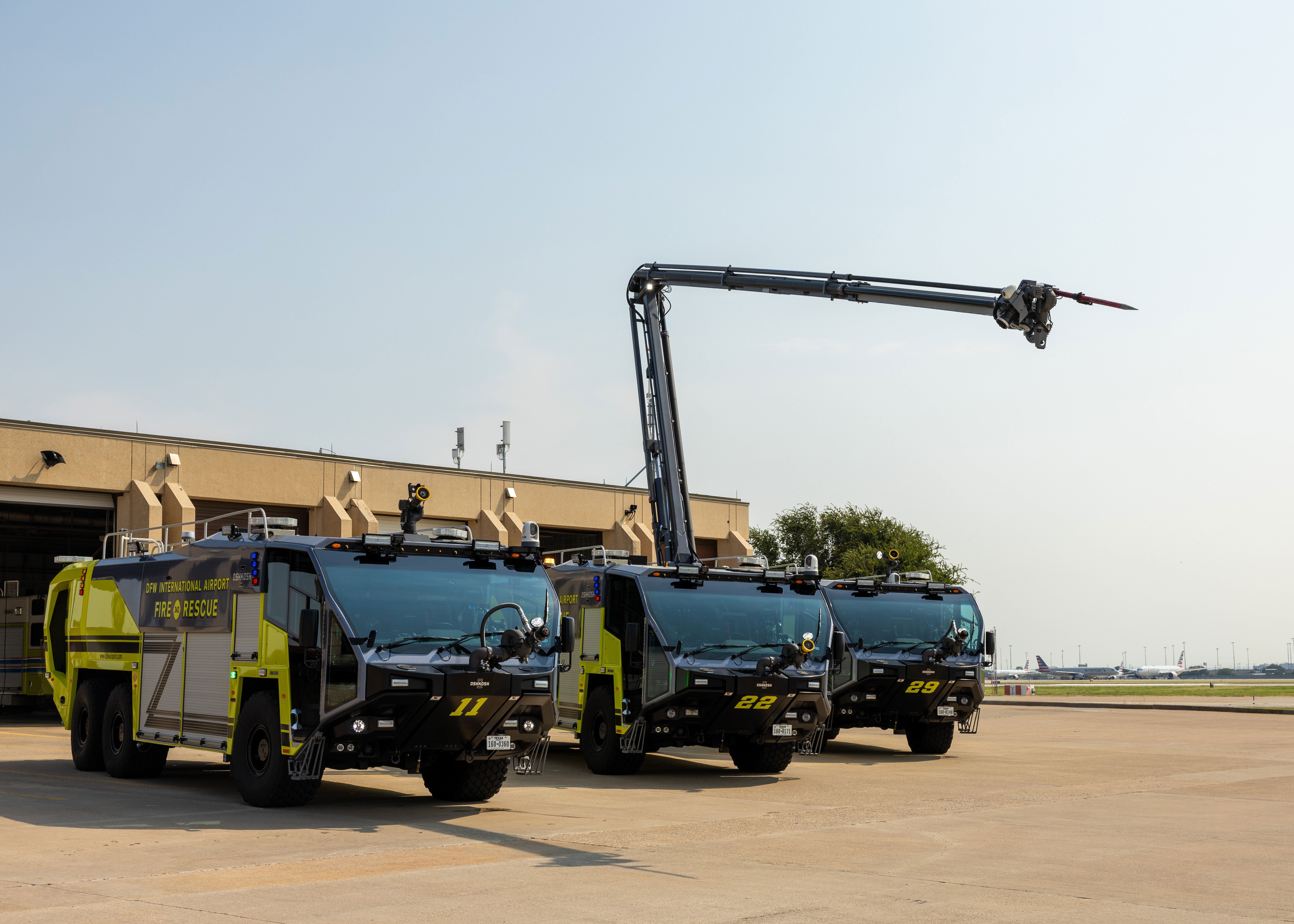 Three Striker ARFF Vehicles parked outside of the DFW Airport Fire Station on a sunny day.