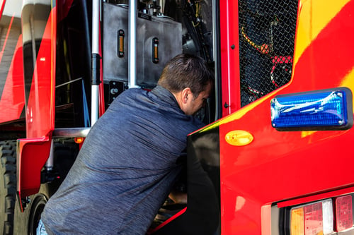 Man working in engine compartment of red Oshkosh Striker ARFF truck.