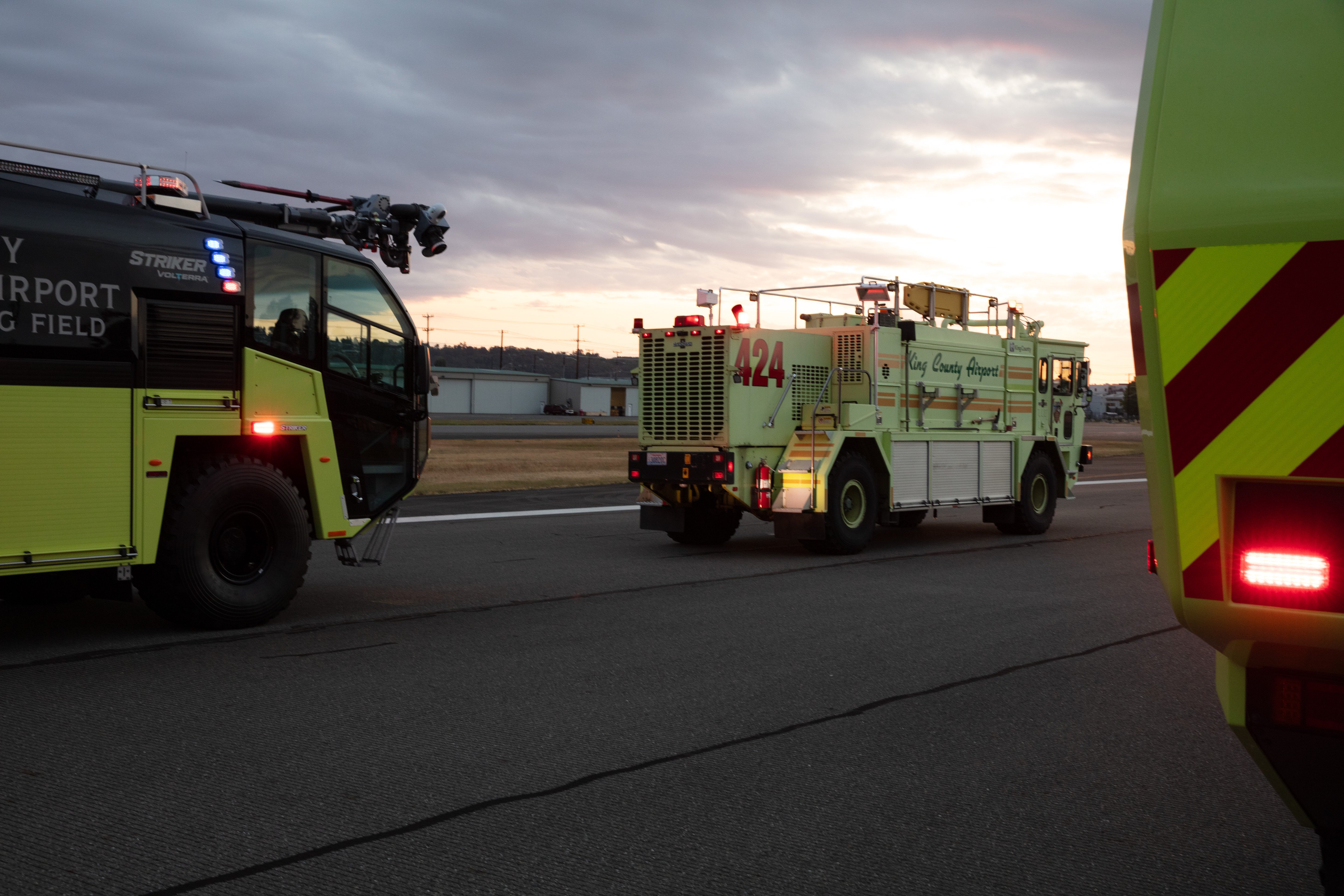 Three Oshkosh ARFF Vehicles driving down the runway at sunset.