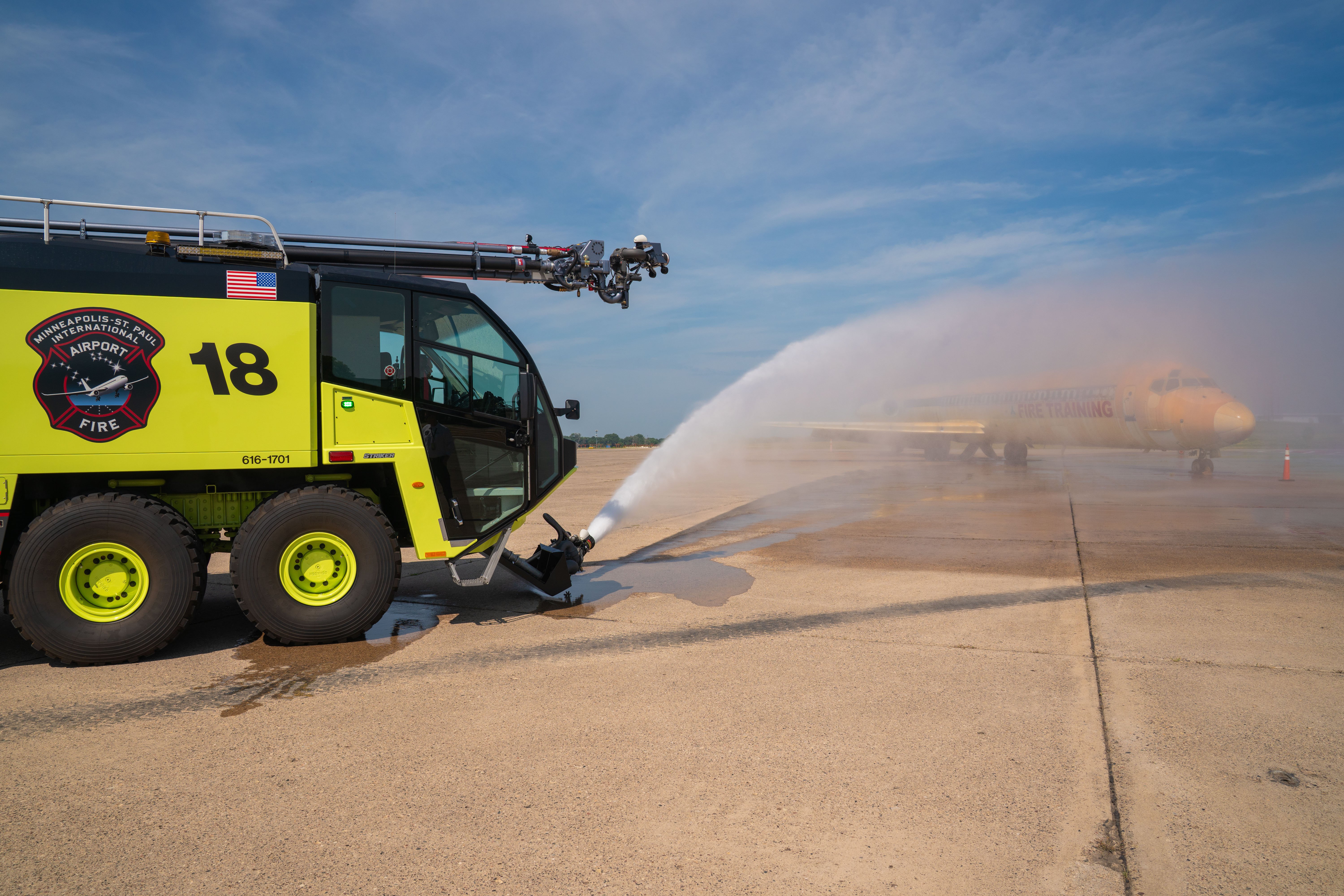 A Striker 8x8 ARFF spraying water from the low attack bumper turret outside on a sunny day.