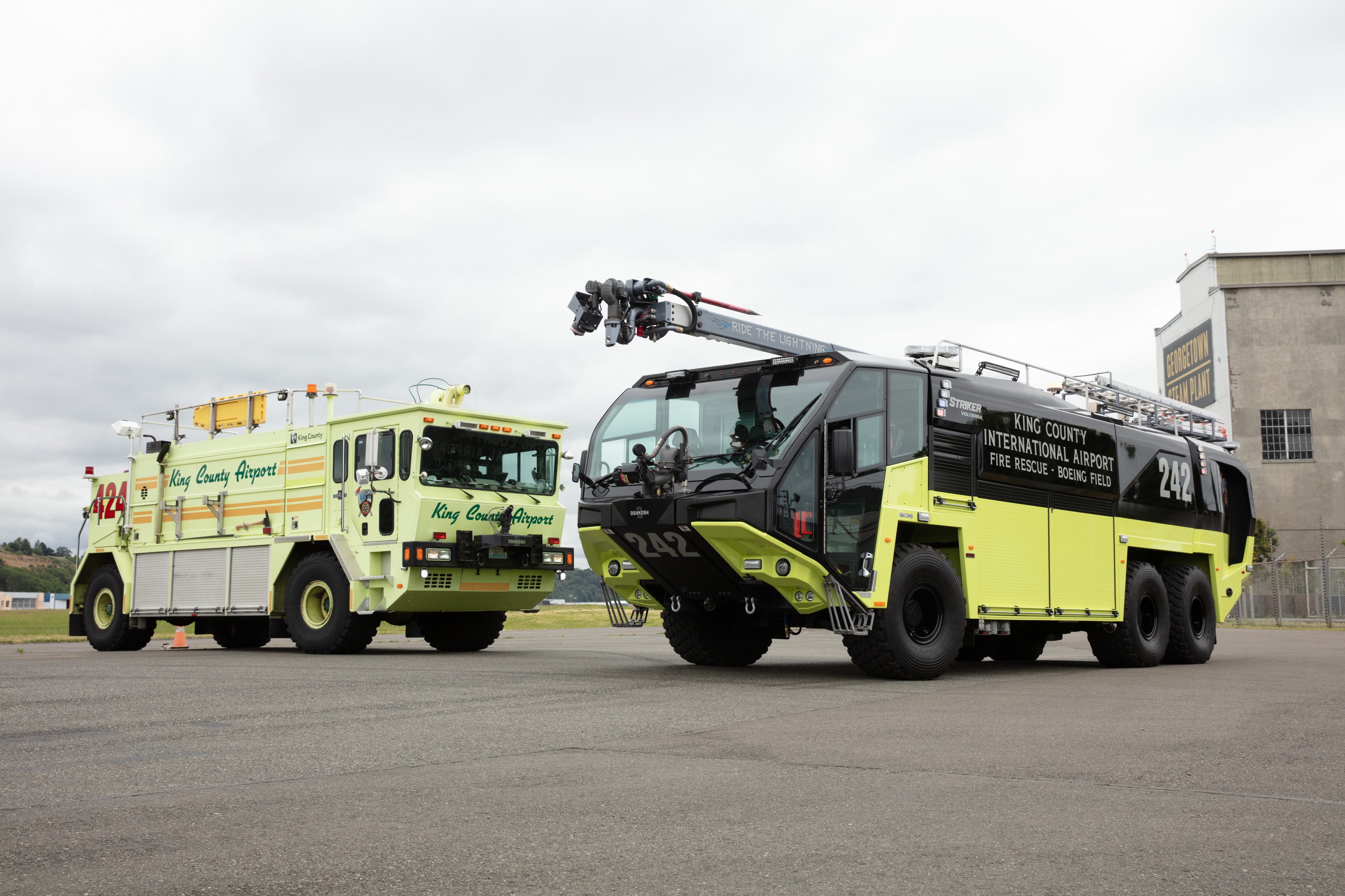 A Striker ARFF and Striker Volterra Electric ARFF parked outside near the airport on a cloudy day.