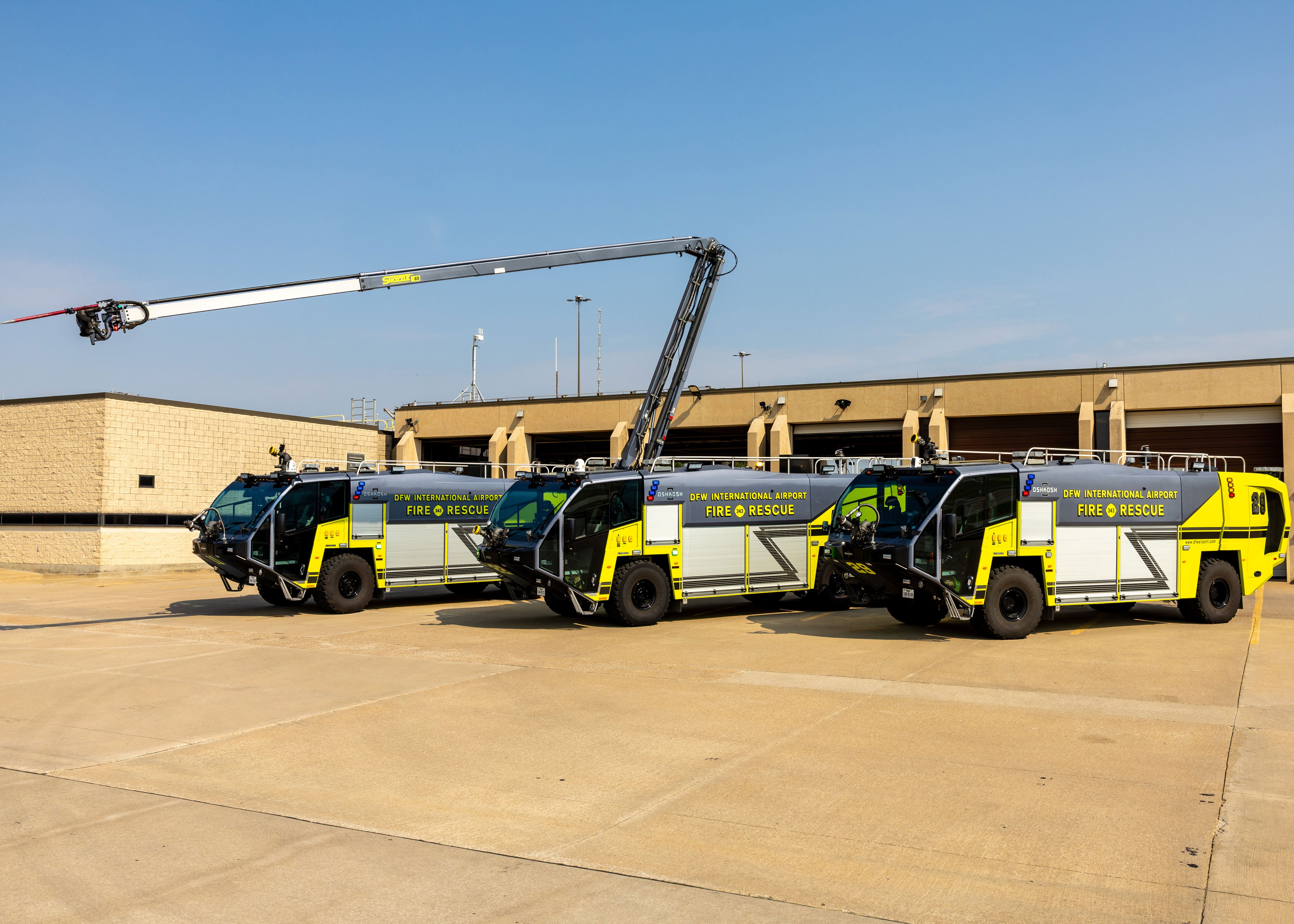 Three Striker ARFF Vehicles parked outside of the DFW International Airport Fire Station on a sunny day.
