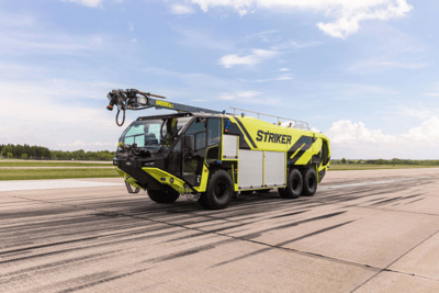 A Striker 6x6 ARFF with a Snozzle high reach extendable turret driving down the runway on a cloudy day.