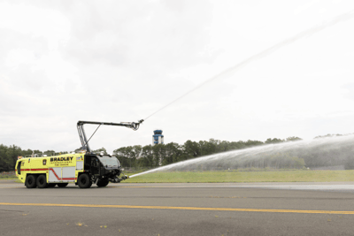 A Striker 6x6 ARFF spraying water from two turrets on a cloudy day.