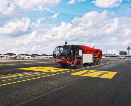 A Striker 6x6 ARFF parked outside at the airport on a cloudy day.