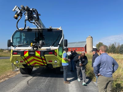 An ARFF truck with people around it, sitting on a country road with a red barn in the background