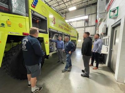 A team of people on a factory floor looking at a neon yellow ARFF truck