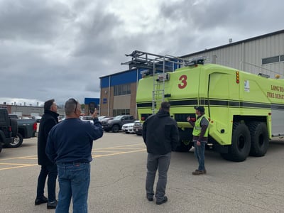 A neon yellow ARFF vehicle sitting outside with a team of people inspecting it