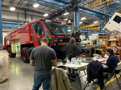A red ARFF truck on the factory floor with a team of people looking at it