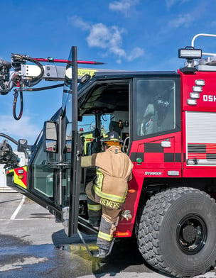 Firefighter climbing into Montreal's new Oshkosh Airport Products Striker 6x6 ARFF vehicle. 