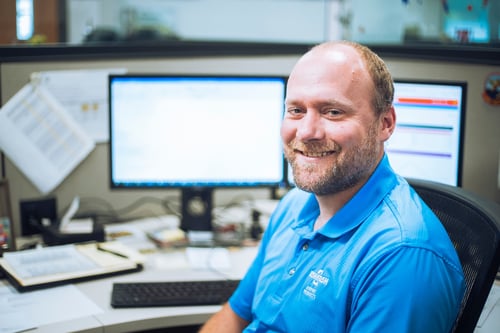 Male Oshkosh Airport Products team member sitting at a desk smiling at the camera.
