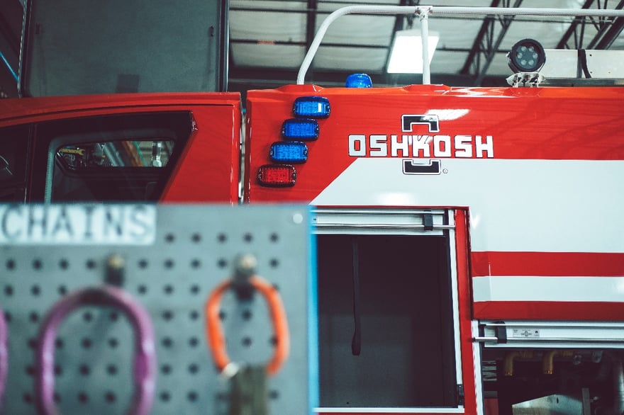 Red Oshkosh Striker ARFF vehicle in the Oshkosh Airport Products facility with a compartment open.