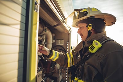 Male firefighter in turnout gear servicing parts in a compartment on a Striker ARFF vehicle. 
