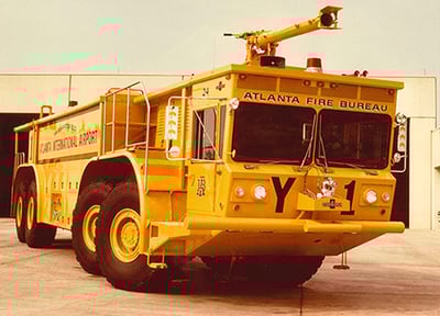 Atlanta Fire Bureau yellow Oshkosh T--Series 8x8 ARFF truck parked outside in front of a fire station.