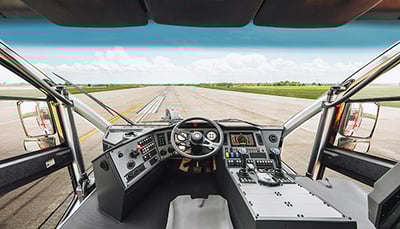 Interior driver’s seat, passenger’s seat and controls in the cab of a Striker ARFF vehicle parked outside on an airport runway.