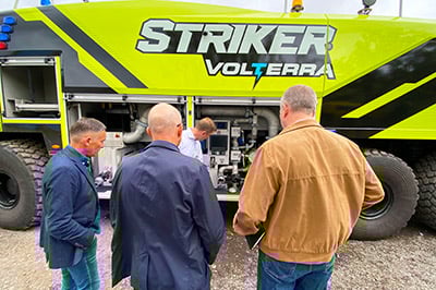 Four men standing beside a Striker Volterra electric ARFF with its compartments open inspecting the vehicle.