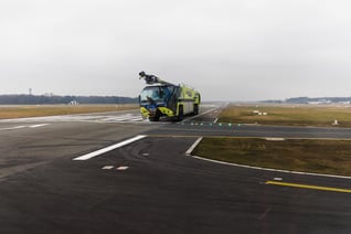 Striker Volterra electric ARFF with a Snozzle high reach extendable turret parked outside on an airport runway on a cloudy day. 