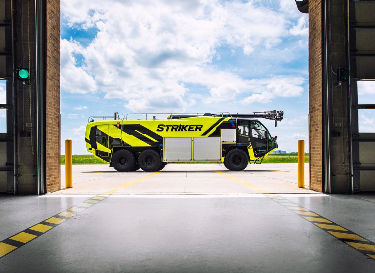 A Striker 6x6 ARFF parked outside of an airport fire station on a cloudy day. 
