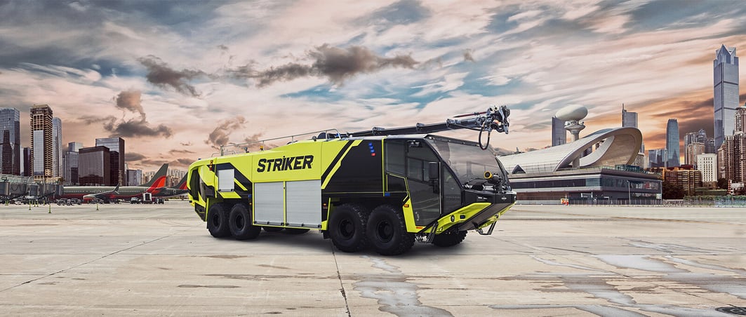 A neon green 8x8 Striker on pavement with a city scape and airplanes in the background.