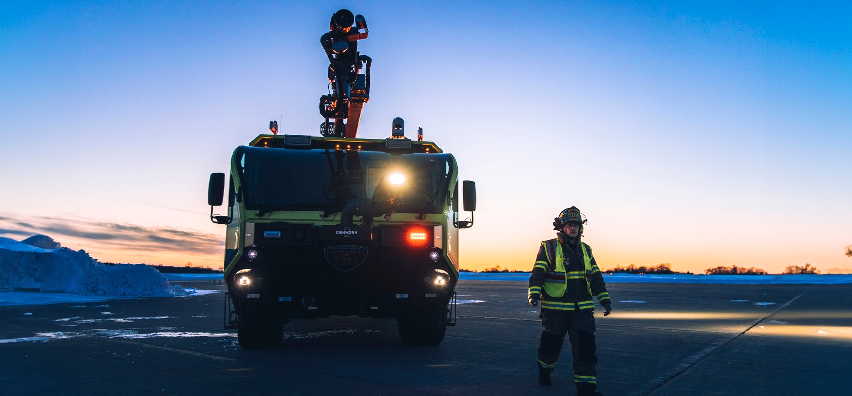 Firefighter standing in front of Striker ARFF vehicle at sunrise.