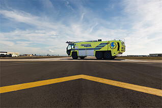 Striker Volterra electric ARFF with a Snozzle high reach extendable turret parked outside on an airport runway on a cloudy day.