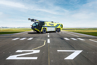 Striker Volterra electric ARFF with a Snozzle high reach extendable turret parked outside on an airport runway on a cloudy day. 