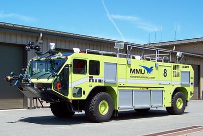 A first generation neon green Striker ARFF truck on pavement in front of a beige building