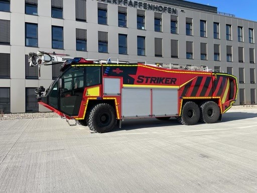 Red Striker ARFF truck parked in front of gray building.