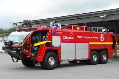 A second generation red Striker ARFF on pavement in front of a building with a gray sky in the background