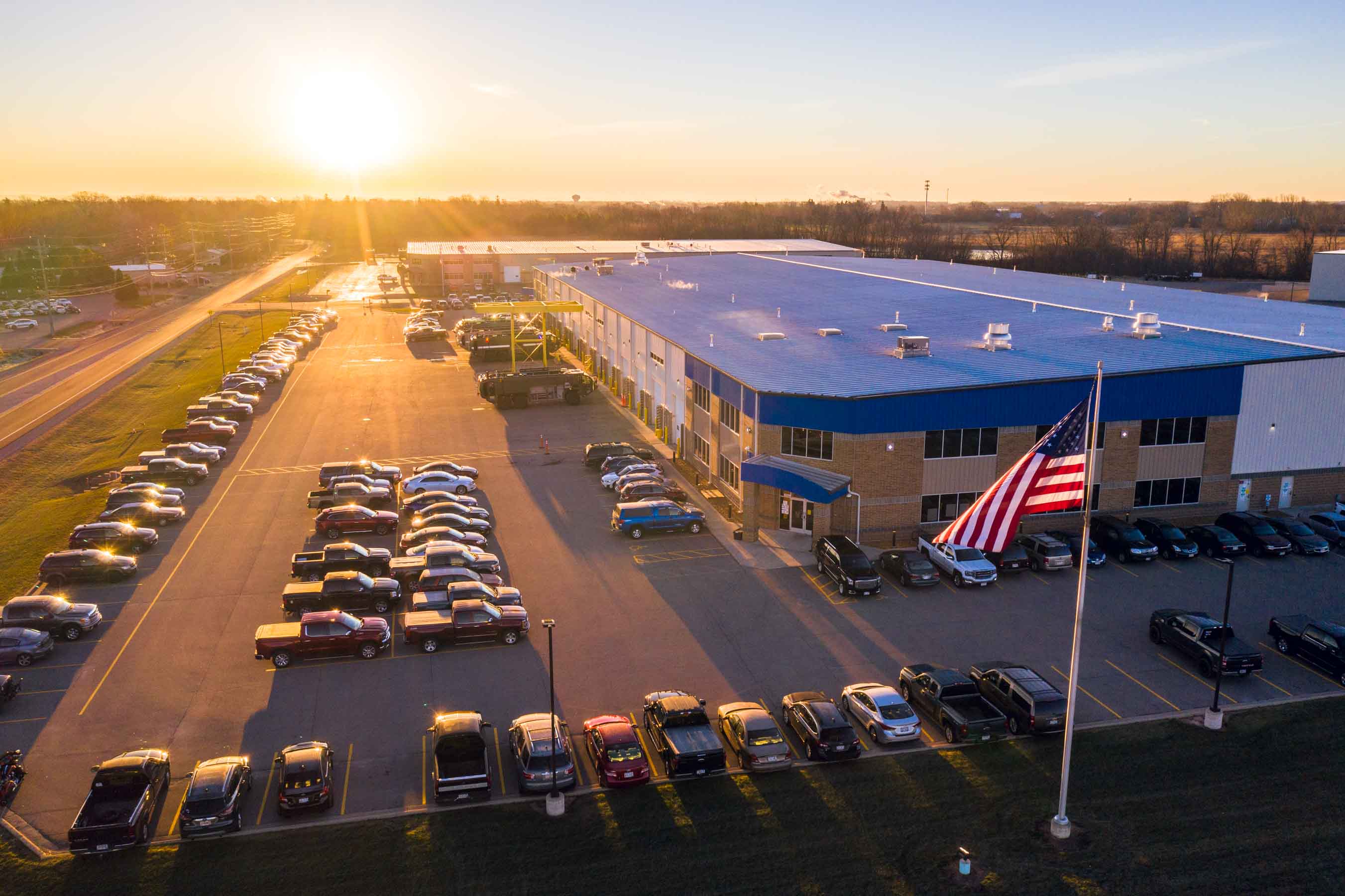 Aerial view of Oshkosh Airport Products manufacturing facility with the sun setting and American flag flying.