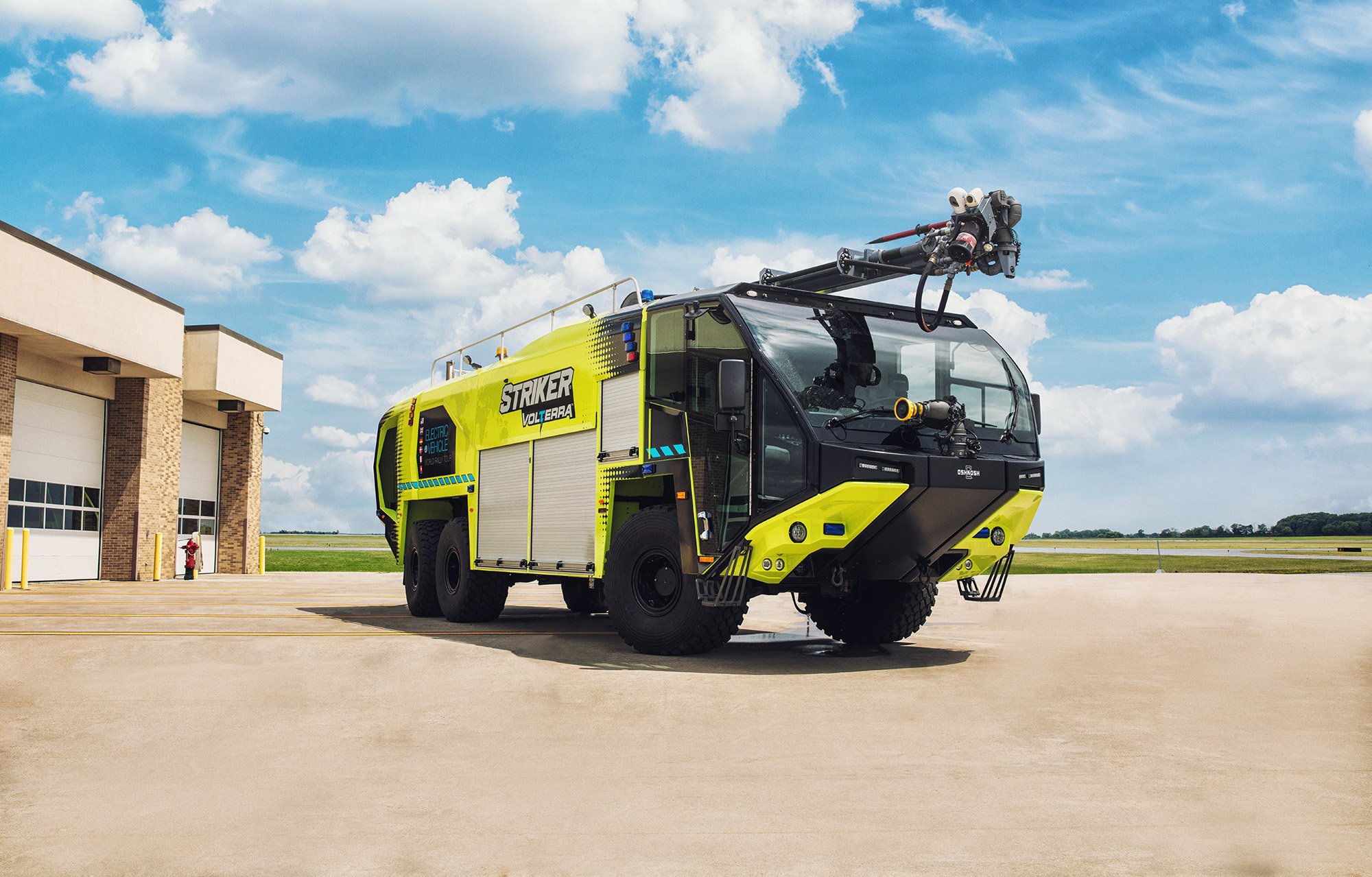 Striker Volterra electric ARFF with a Snozzle high reach extendable turret parked outside near the airport fire station on a sunny day. 