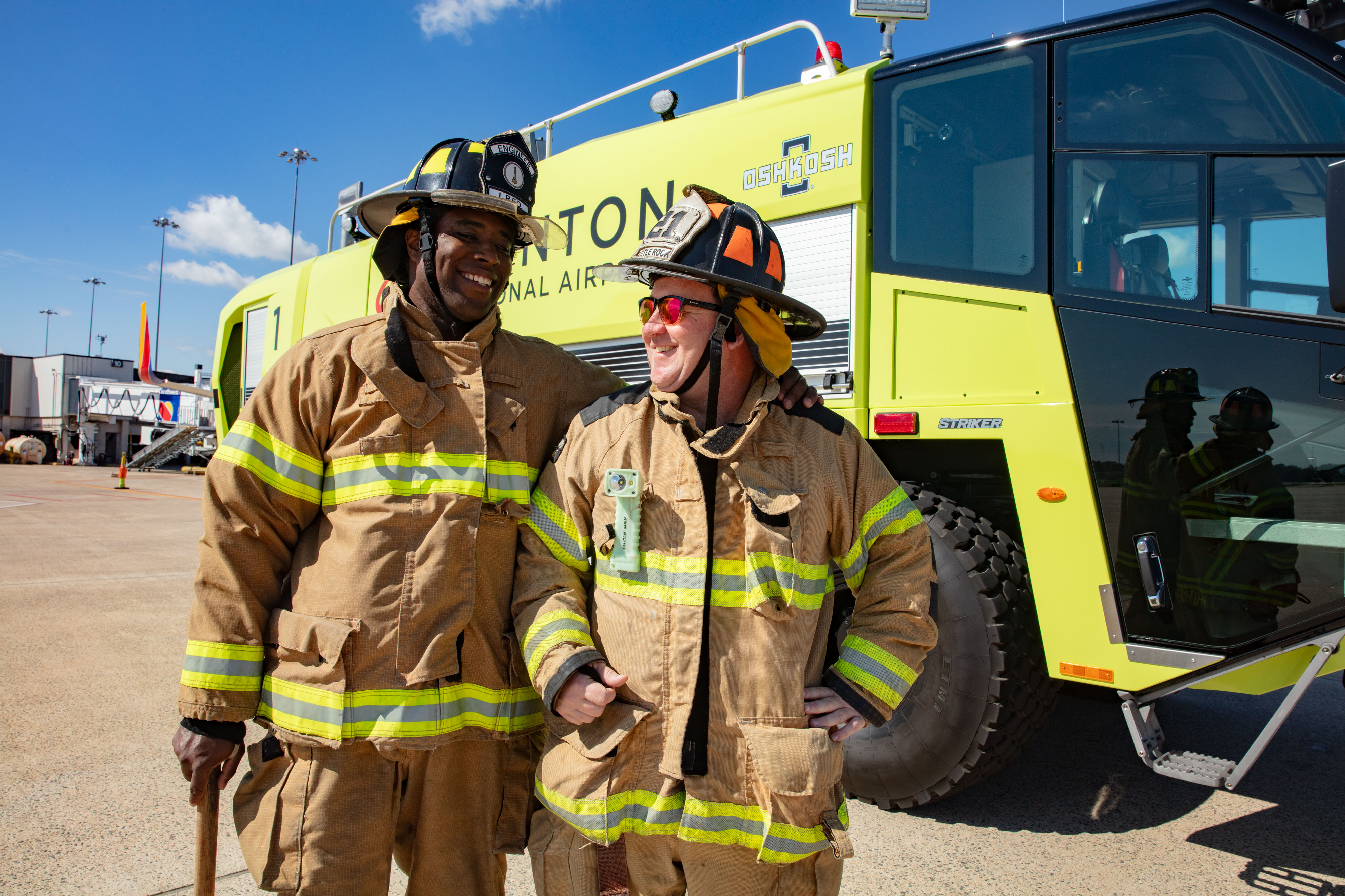 Two ARFF Firefighters standing beside a Striker 4x4 ARFF on a sunny day.