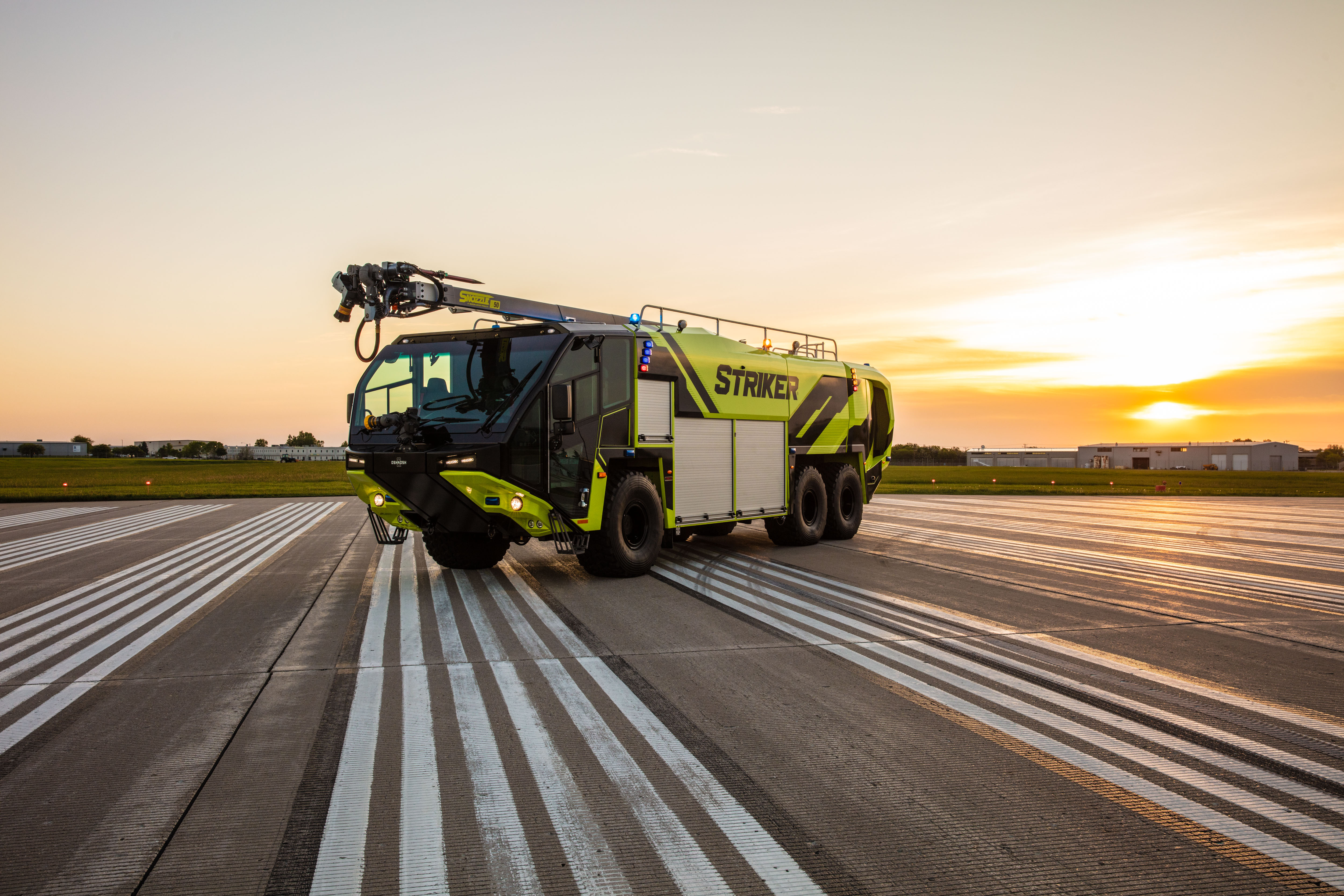A Striker 6x6 ARFF with a Snozzle high reach extendable turret parked outside on the runway at sunset.