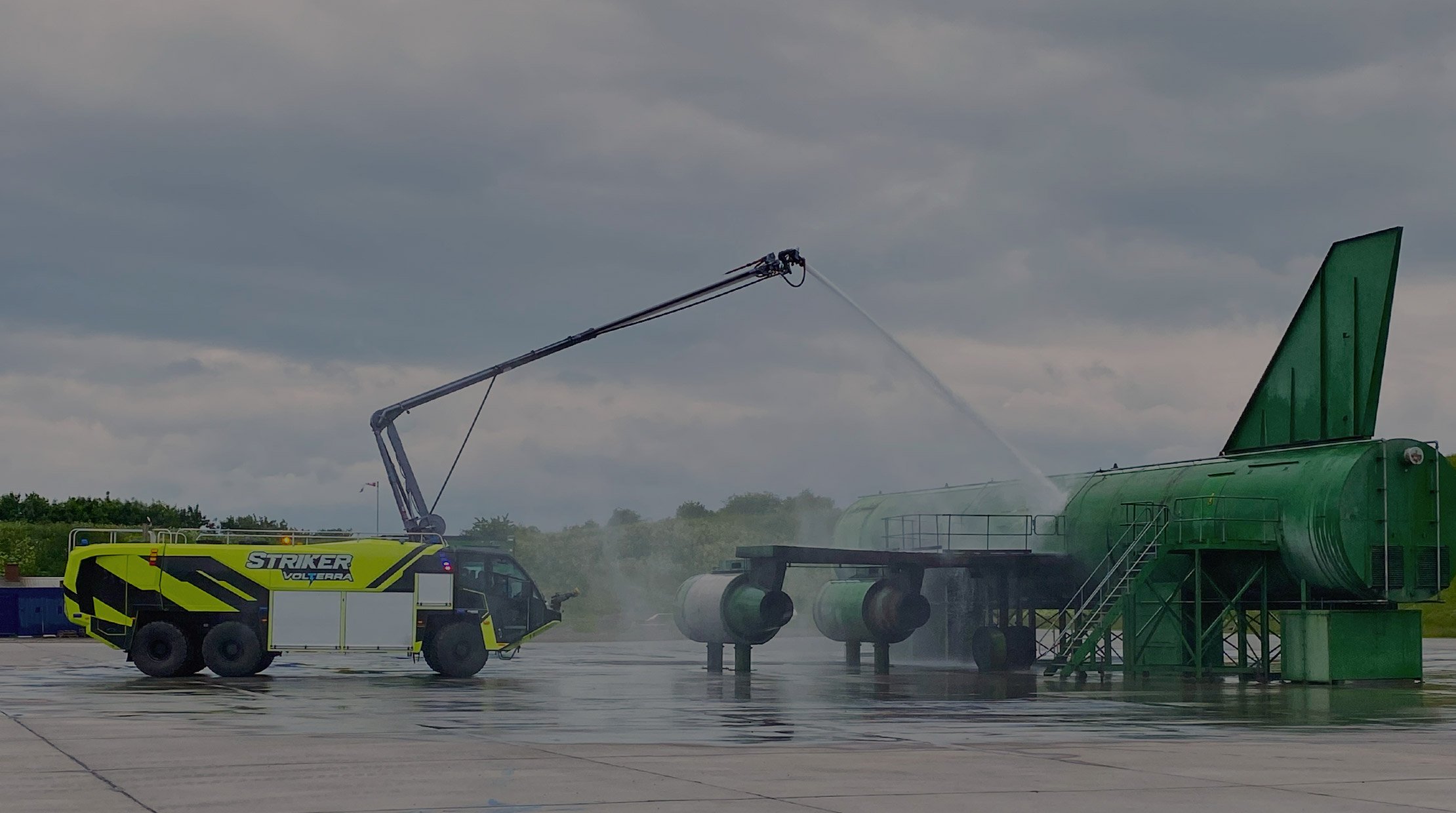 Oshkosh Striker Volterra ARFF Vehicle spraying water on airplane.