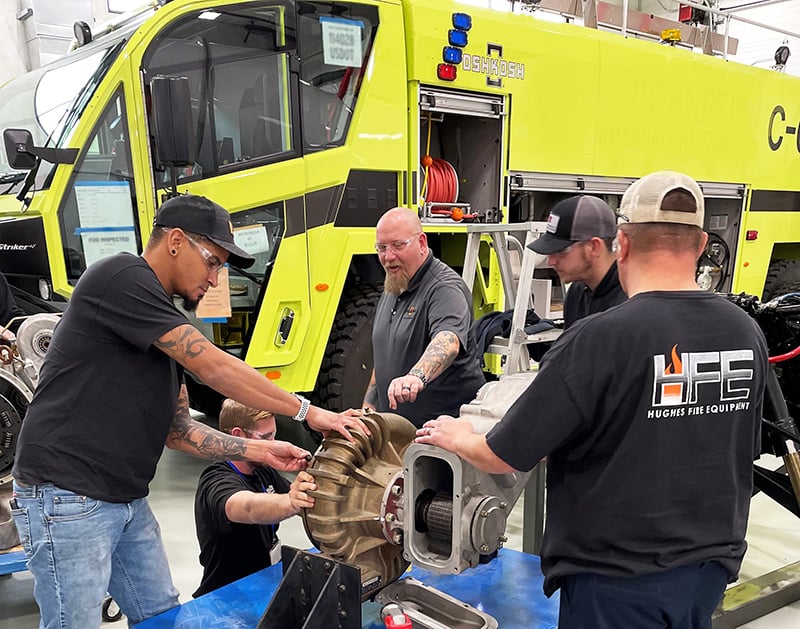 Five men training near a Striker ARFF vehicle inside the manufacturing facility. 