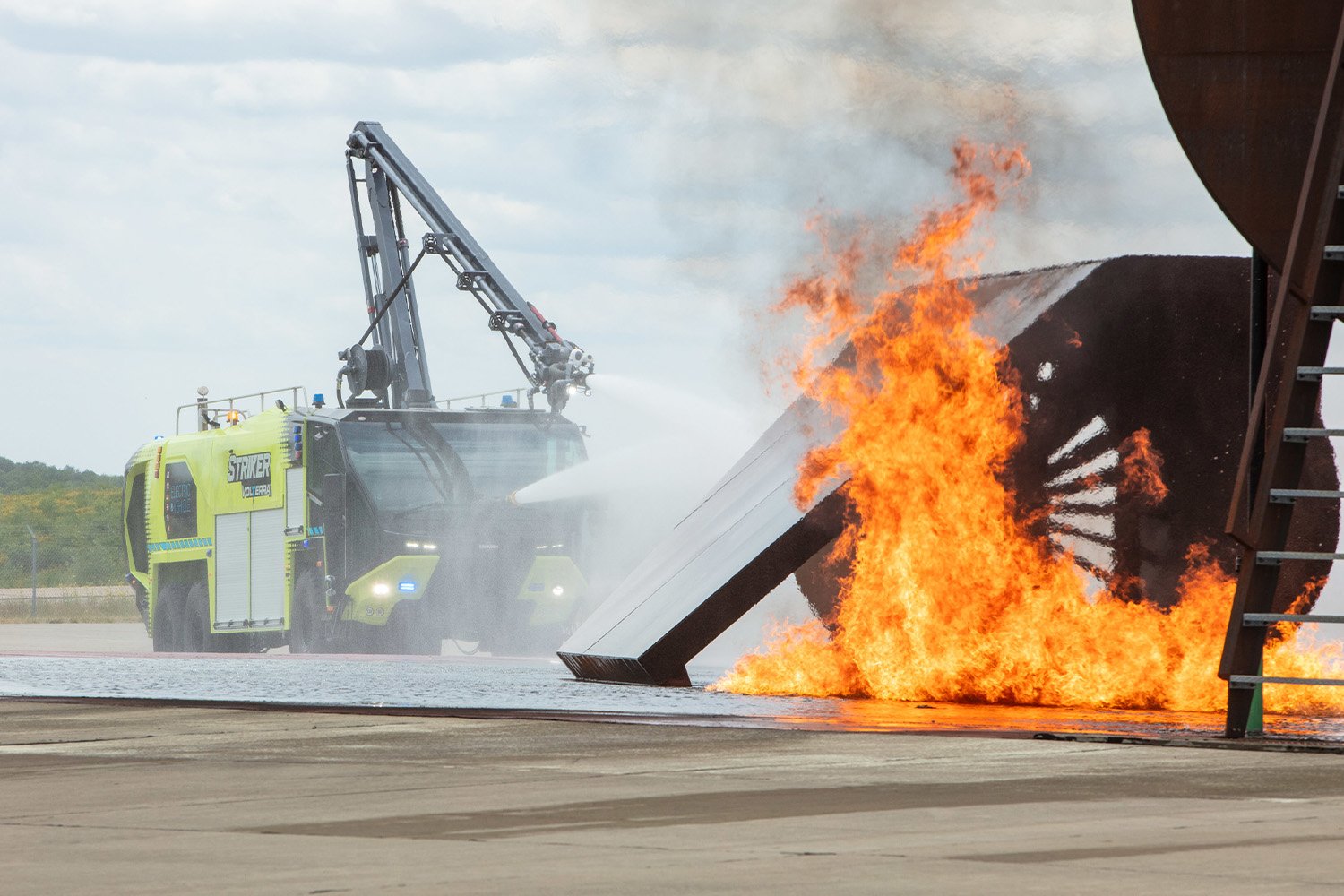 A Striker Volterra electric ARFF with the Snozzle high reach extendable turret extended spraying water at a fire scene at an airport. 