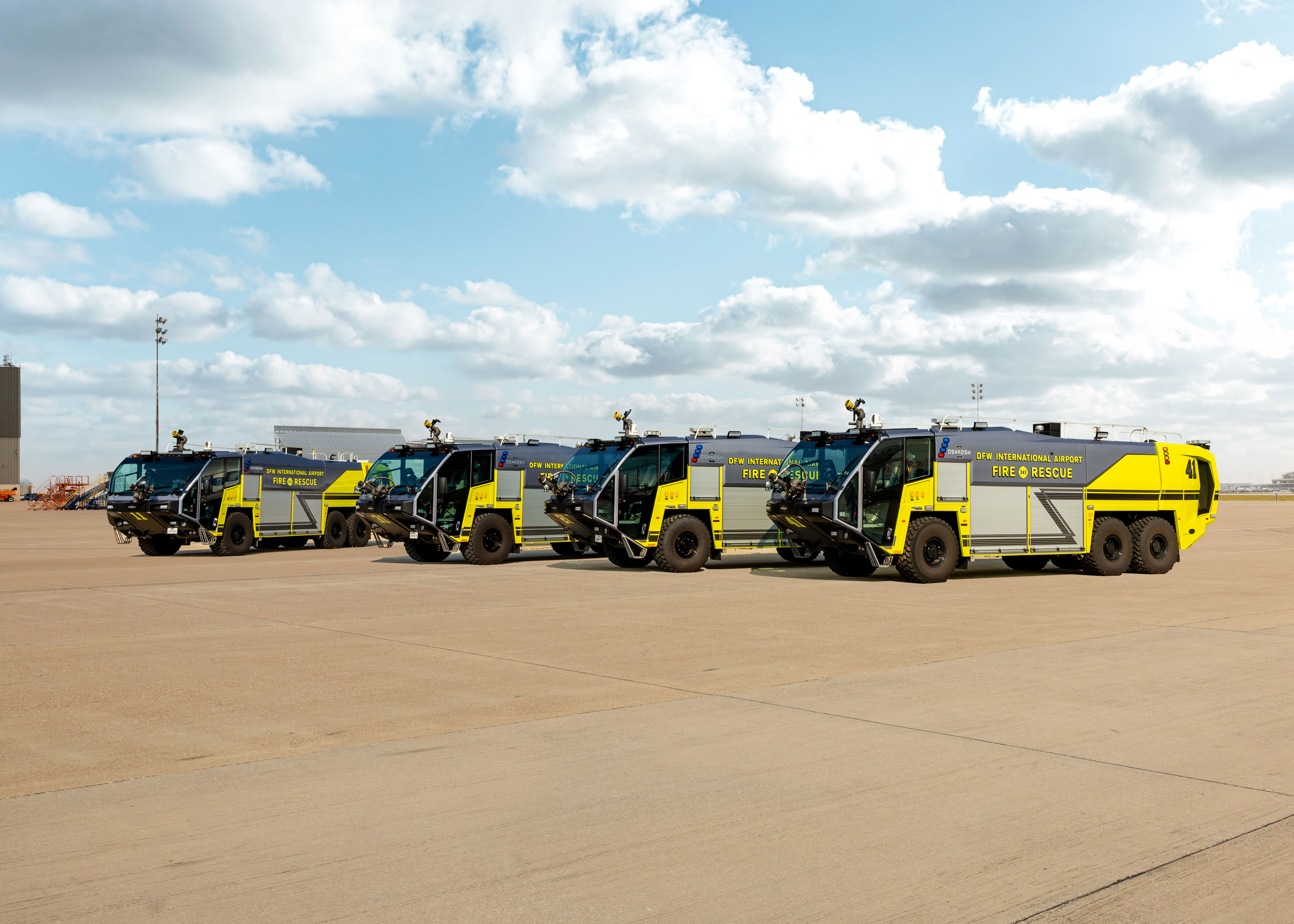 Four Striker ARFF Vehicles parked outside at DFW International Airport on a cloudy day.